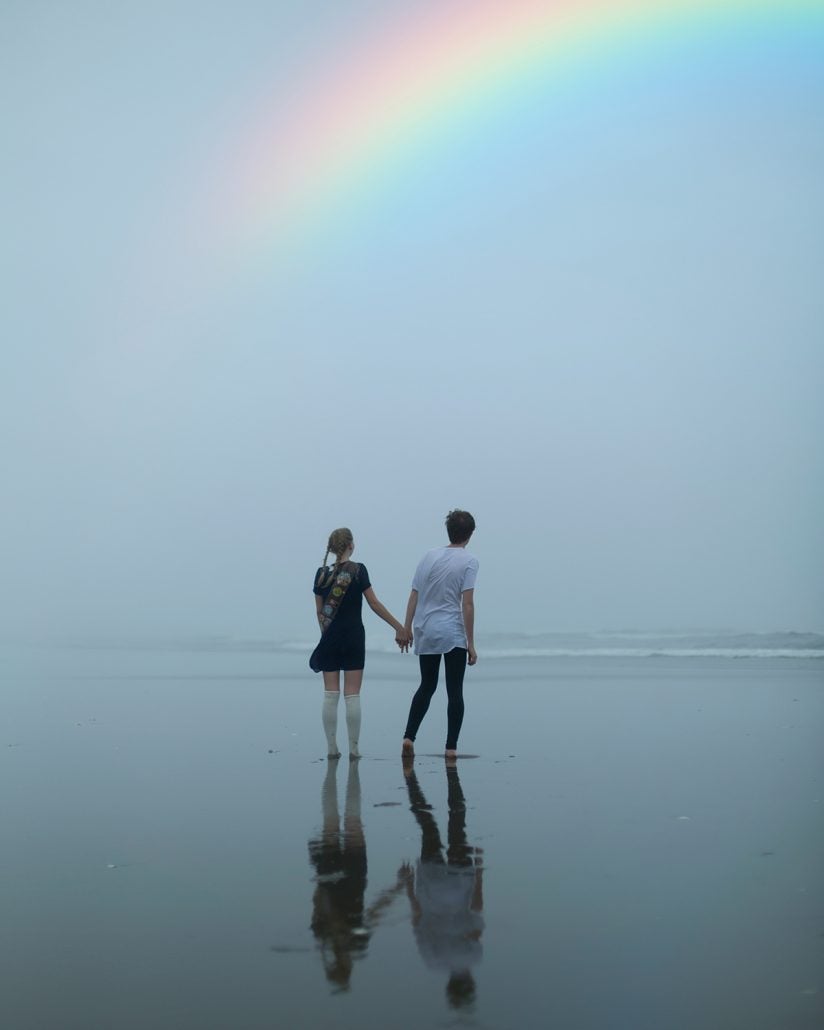 rainbow in cloudy sky over two people holding hands
