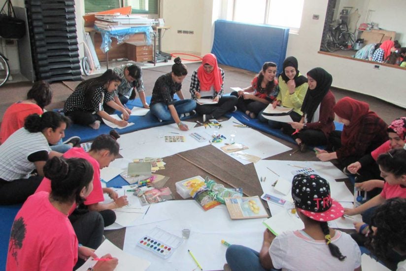 Fifteen young women sitting in circle on floor working on art projects
