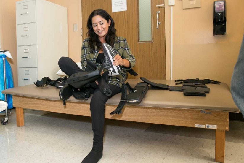 Cynthia Ramirez seated, putting on robotic exoskeleton