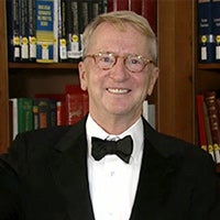 David C. Bohnett in a white button-down suit, black bowtie and black suit jacket with a bookcase in the background
