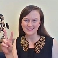 Rachel Morford in a black dress with gold lace pattern on the color holding two fingers up in the USC victory sign