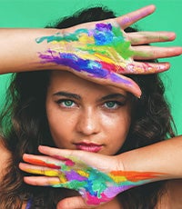Gwenan Walker framing her face with her hands with vibrant multicolored paint on her palms