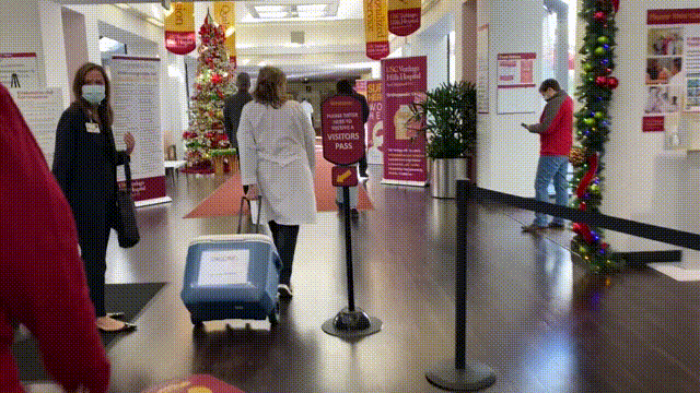 A woman in a white lab coat rolling a cooler with vaccine doses into the lobby of USC Verdugo Hills Hospital