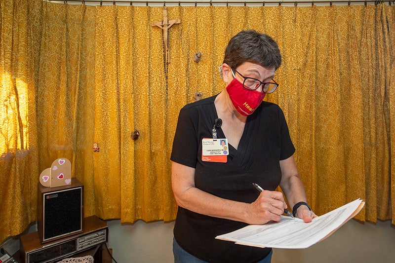 Laura Mosqueda in a black t-shirt and red USC facemask marking a medical form in a patient’s home