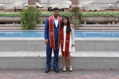 Anjali Krishna Prasad and Vipin Dwivedi in formal clothing and USC graduation sashes in front of reflecting pool at Leavey Library.