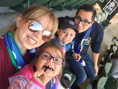 USC alumni Jessica and Renne Sanchez sit in bleacher seats with their young children.