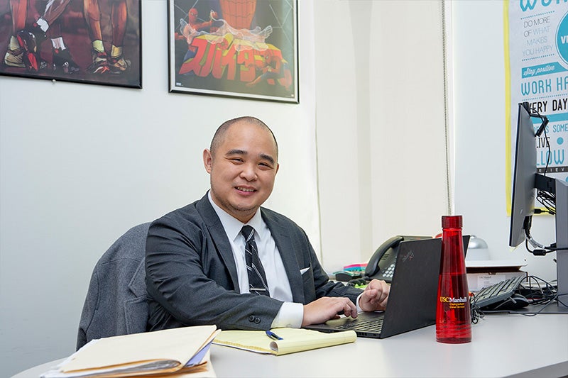 Portrait of Jason Tran in his office at the USC Marshall School of Business wearing a dark gray suit and light blue shirt