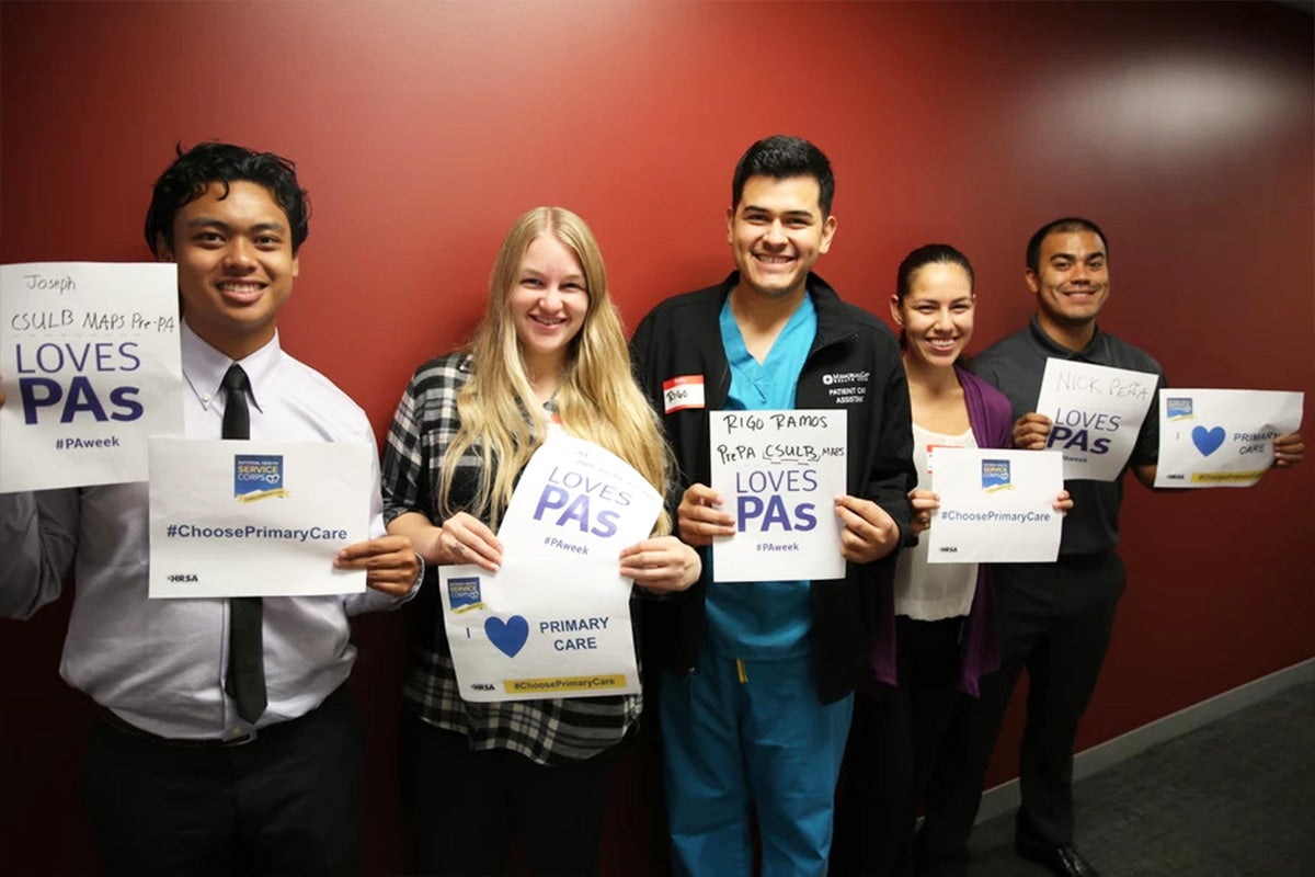 Five students stand in a row holding up signs promoting Physicians Assistant week.