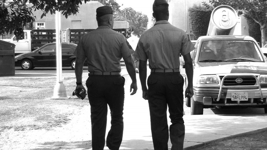 Black and white photo of two military service men walking away from the camera on a city street.