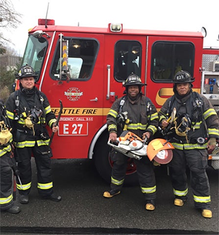 Image of Seattle firefighters standing in front of a fire truck holding heavy-duty tools.