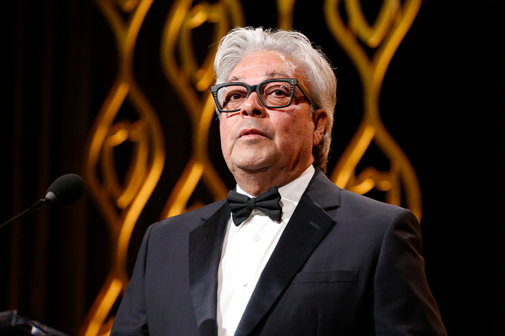 White-haired man wearing glasses and a bow tie receives award