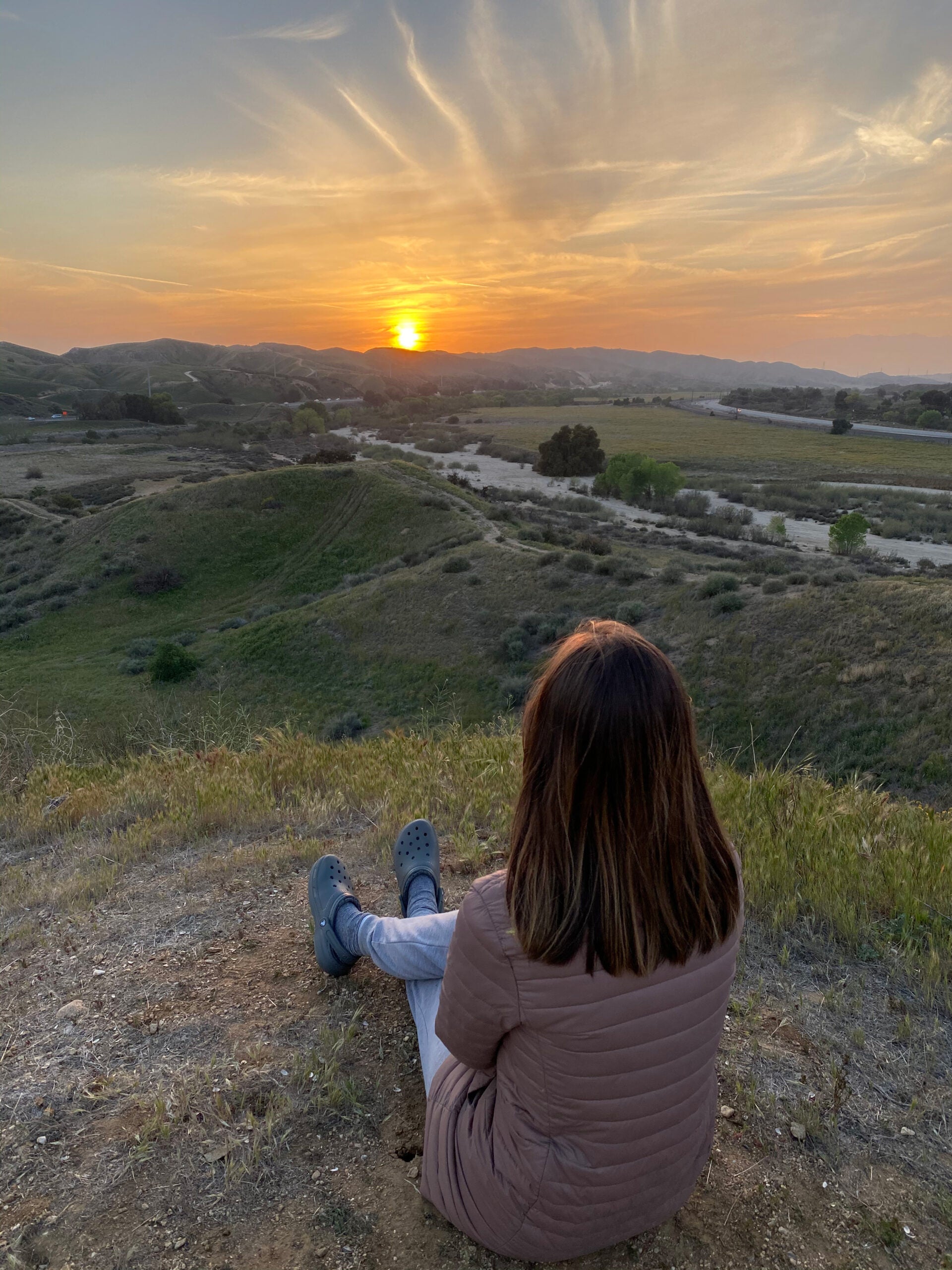 Woman sits on top of a hill watching a sunset.