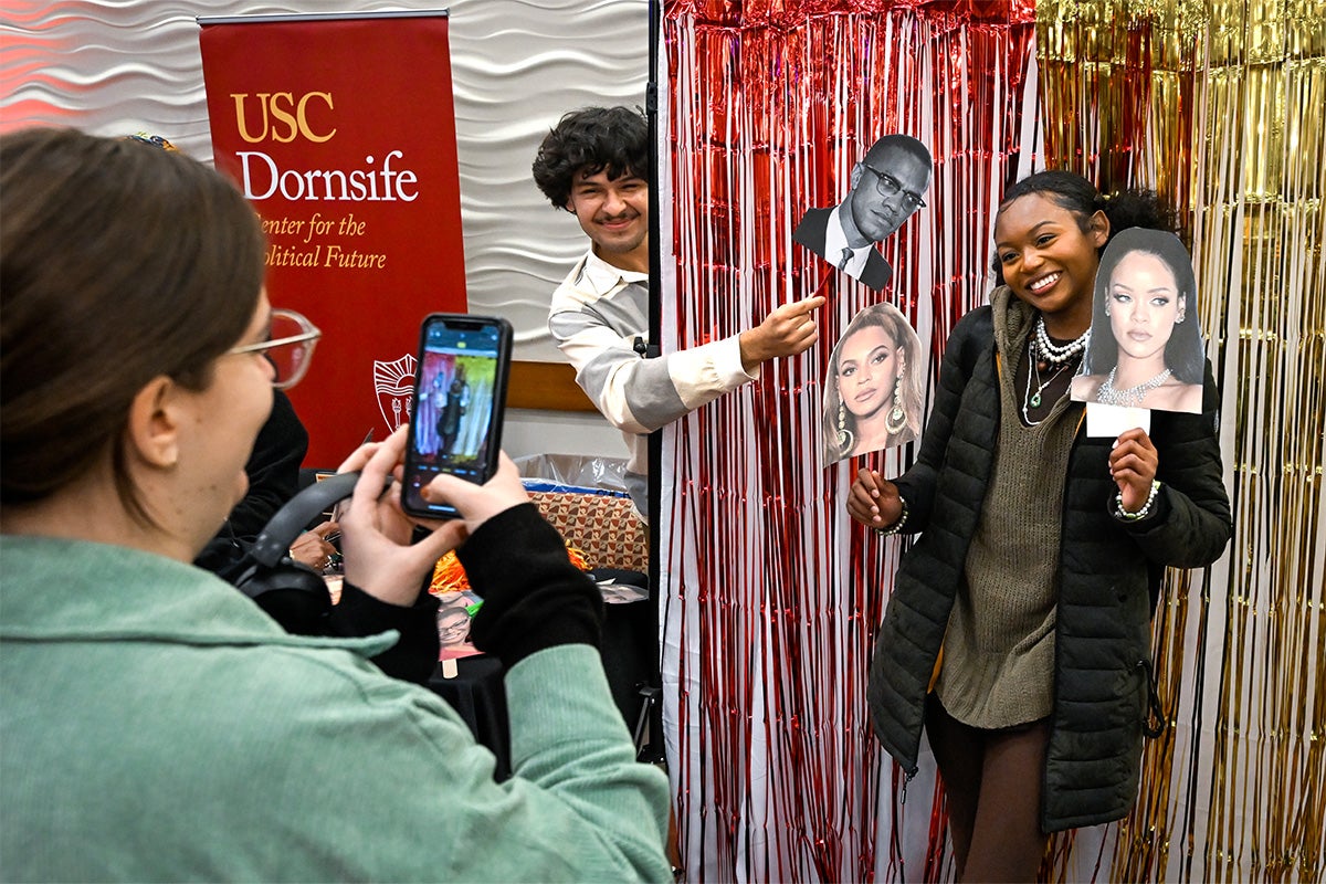 Nicole Pompilio taking a photo of Gabe Romero and Jamilah Muhammad holding up pictures of famous Black figures.