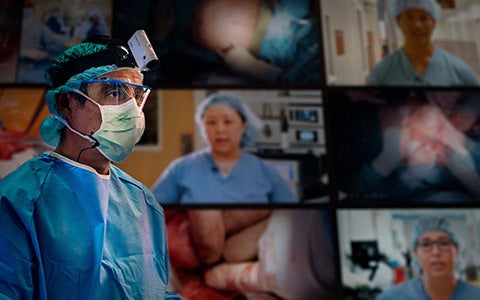 A surgeon watches medical procedures on video screens.