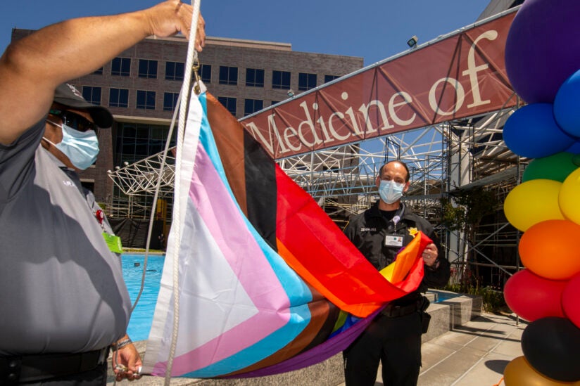 Two men about to raise a Pride Progress flag in front of the Keck Hospital of USC