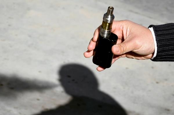 Individual holding a vape over a sidewalk