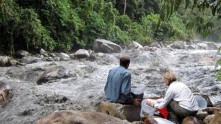 USC Dornsife's Josh West, left, and Sarah Feakins sample water for analysis by a raging river