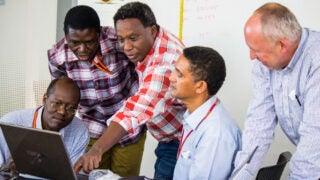 Researchers gathered together and man pointing to something on a laptop