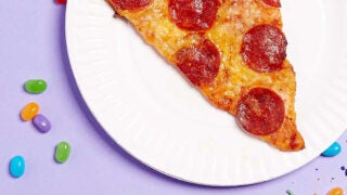 Slice of pizza on a paper plate surrounded by jellybeans