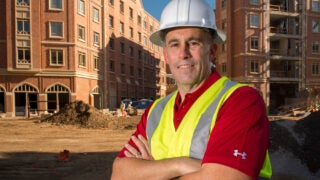 Man with yellow vest and hard hat in front of construction site