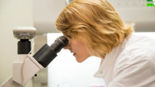 Woman in white lab coat looking inside microscope