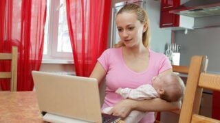 Young mother holding baby and looking at her laptop