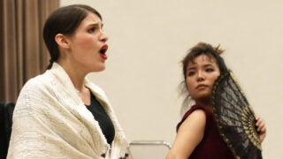 Woman singing next to another woman with a large fan