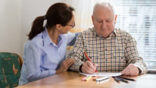 A women helping an older man coloring on paper.