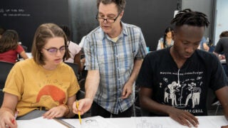 Two students working at a desk with a professor instructing them