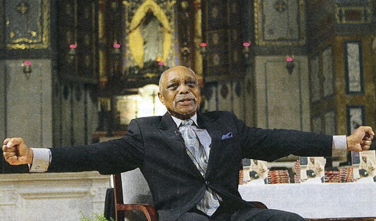 Man with arms spread out sitting in a chair next to a dining table