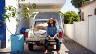 Long-haired man sitting on the bed of a pick-up truck