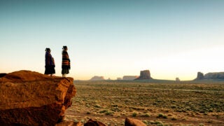 woman wrapped in blankets overlooking a sunset in the desert