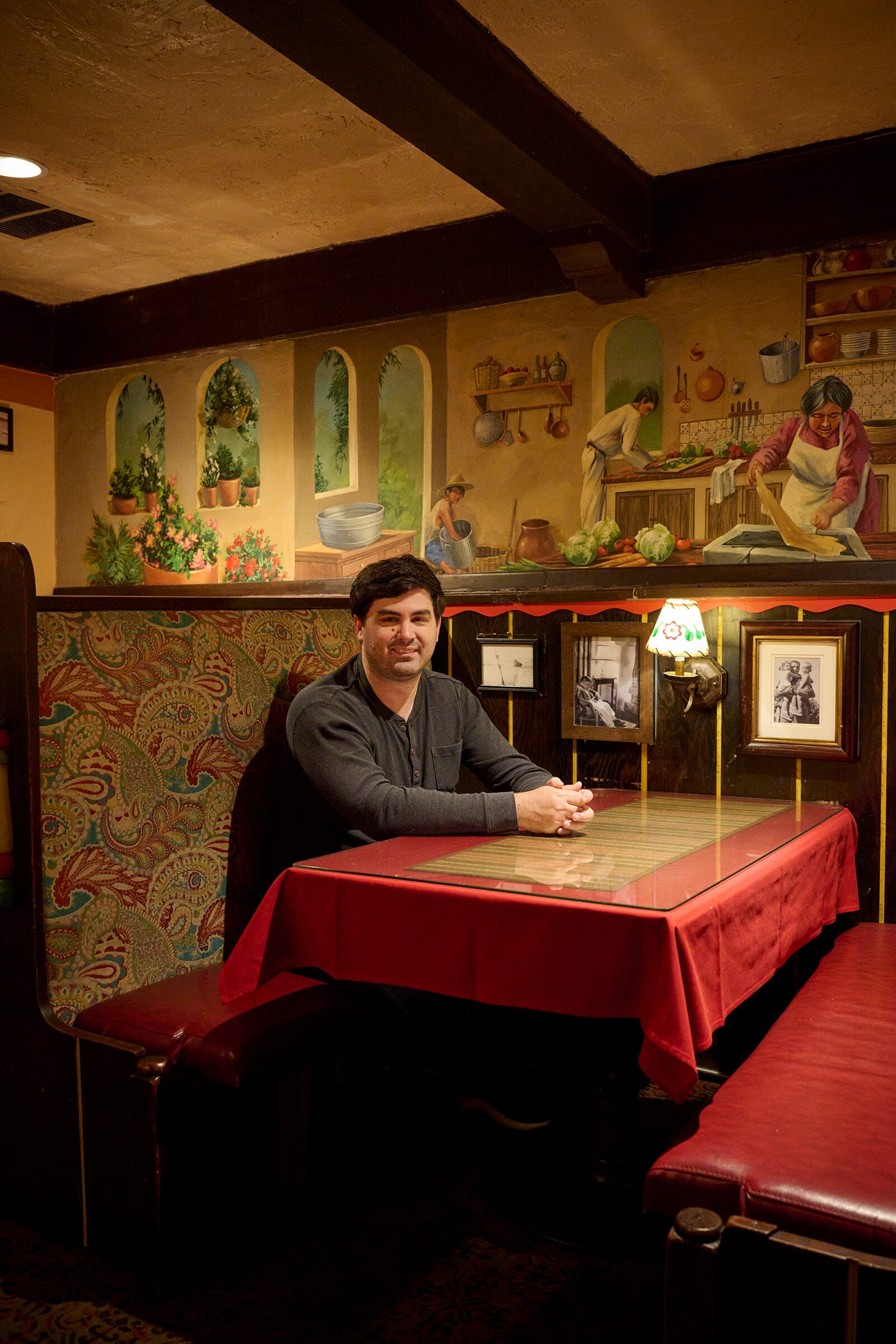 Man in a gray shirt sitting in a red booth in front of a mural on the wall above.