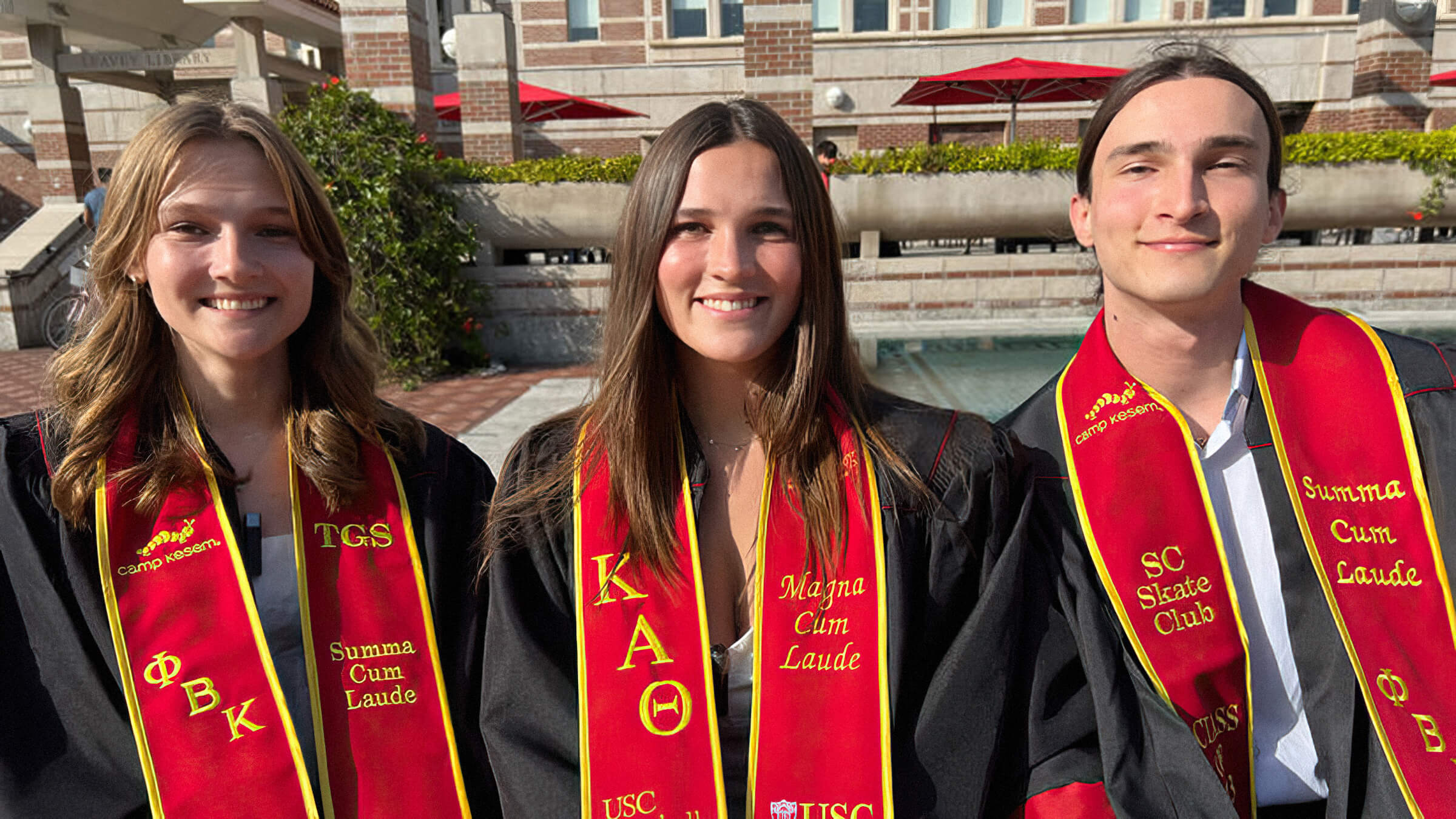 A photo of triplets in USC graduation gown and sash in front of Leavey Library.