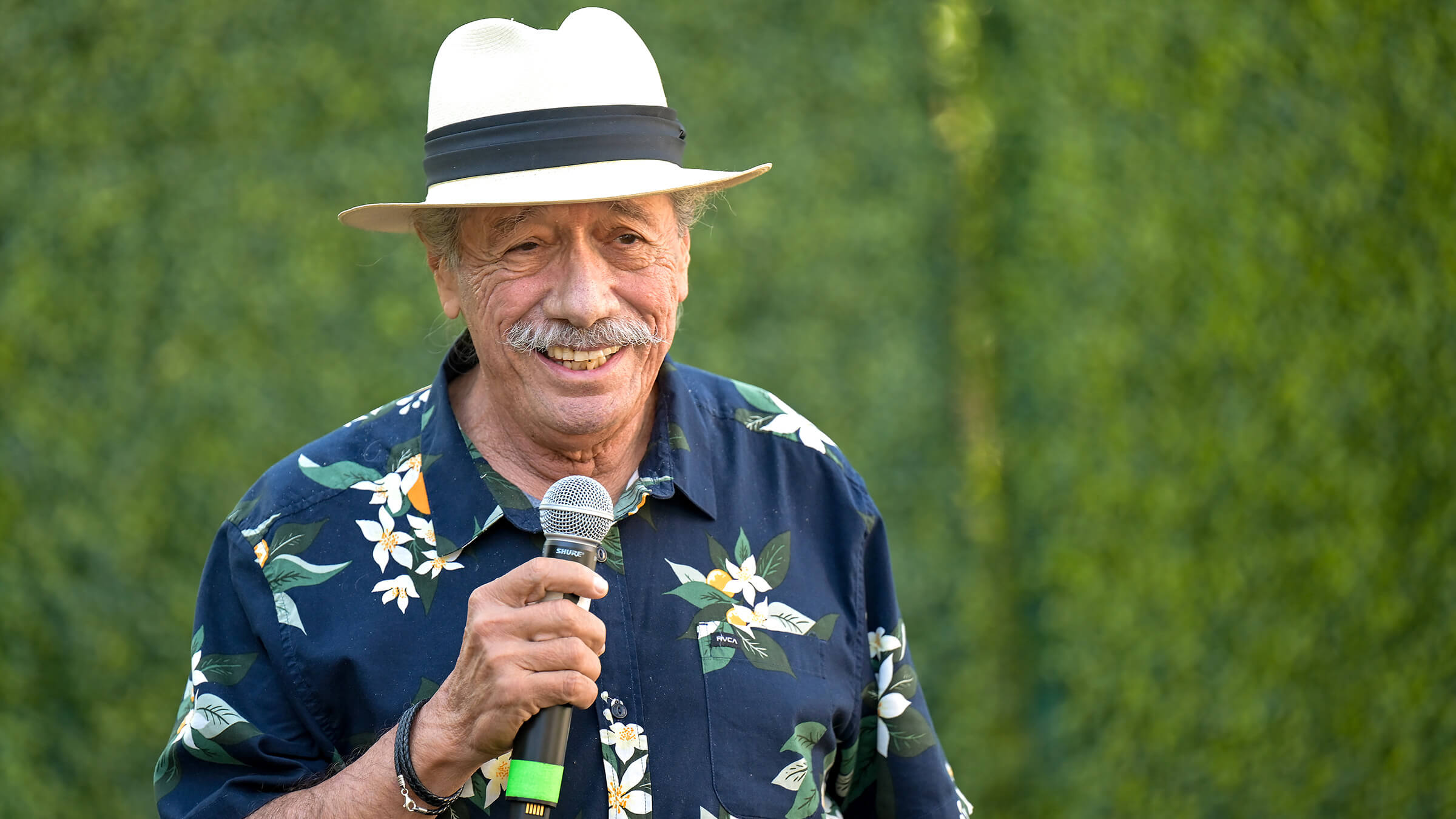 James Olmos speaking, wearing a hat and flowered patterned blue shirt.