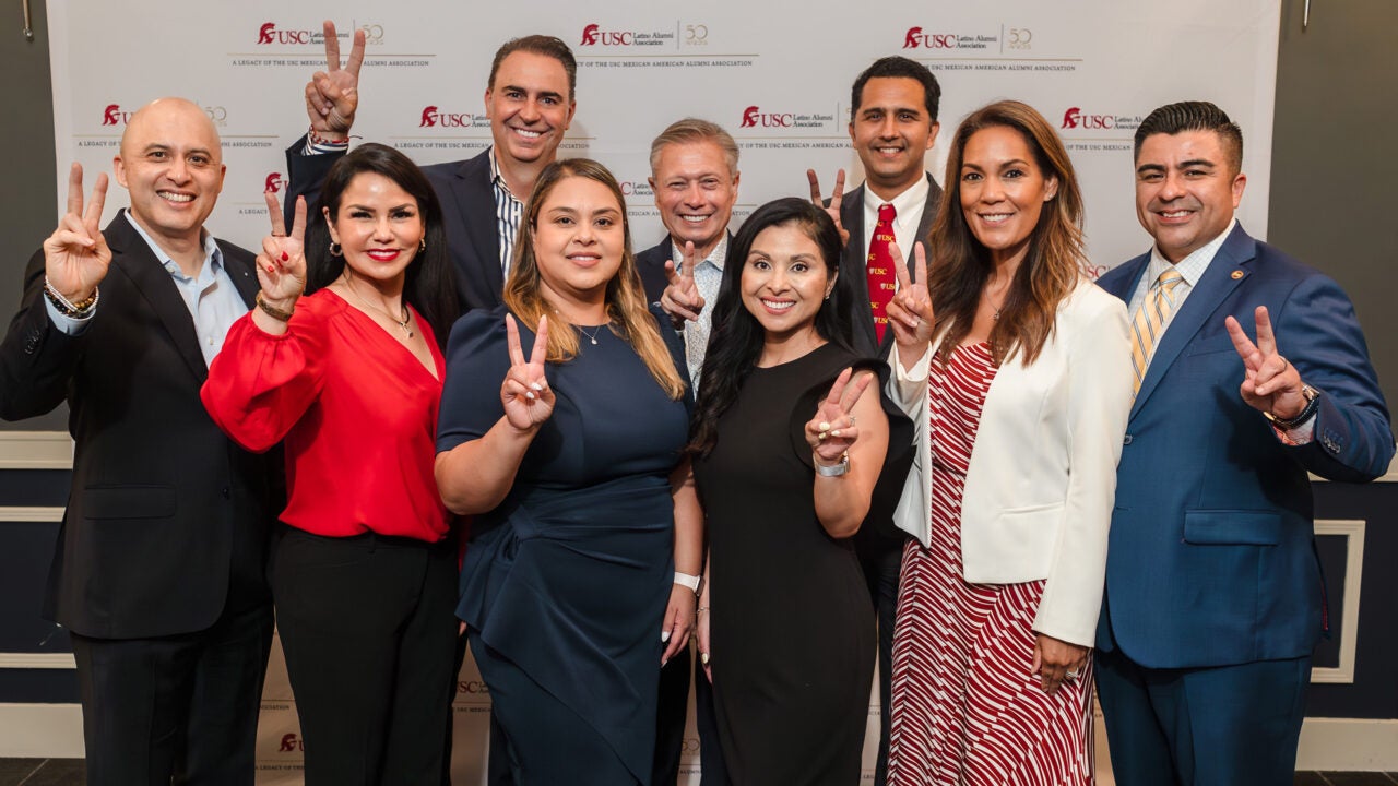 A group of Latino men and women who are USC alumni giving the Fight On hand signal 