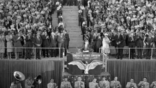 In this July 15, 1960, file photo, Sen. John F. Kennedy gets a standing ovation as he steps to the speaker's podium to accept the Democratic party's nomination for president in the Los Angeles Coliseum in California. Standing in the first row at right is his mother, Rose Kennedy, and next to her is Sen. Lyndon B. Johnson, the vice-presidential candidate.