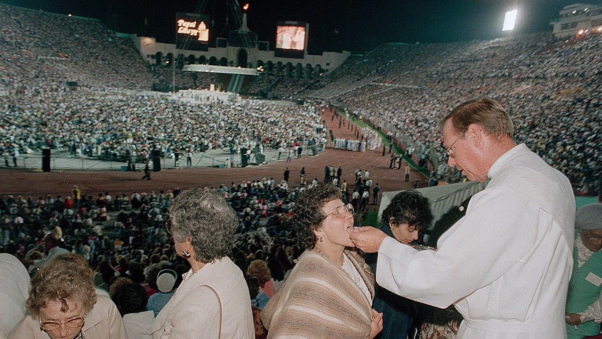 Communion is given to part of the crowd of more than 100,000 people attending Mass with Pope John Paul II at the Los Angeles Memorial Coliseum, Calif., Tuesday evening, September 15, 1987. The Pope told the crowd that California leads the nation in many.  ways, but that progress "it creates new possibilities for evil as well as good." (AP Photo/Reed Saxon)