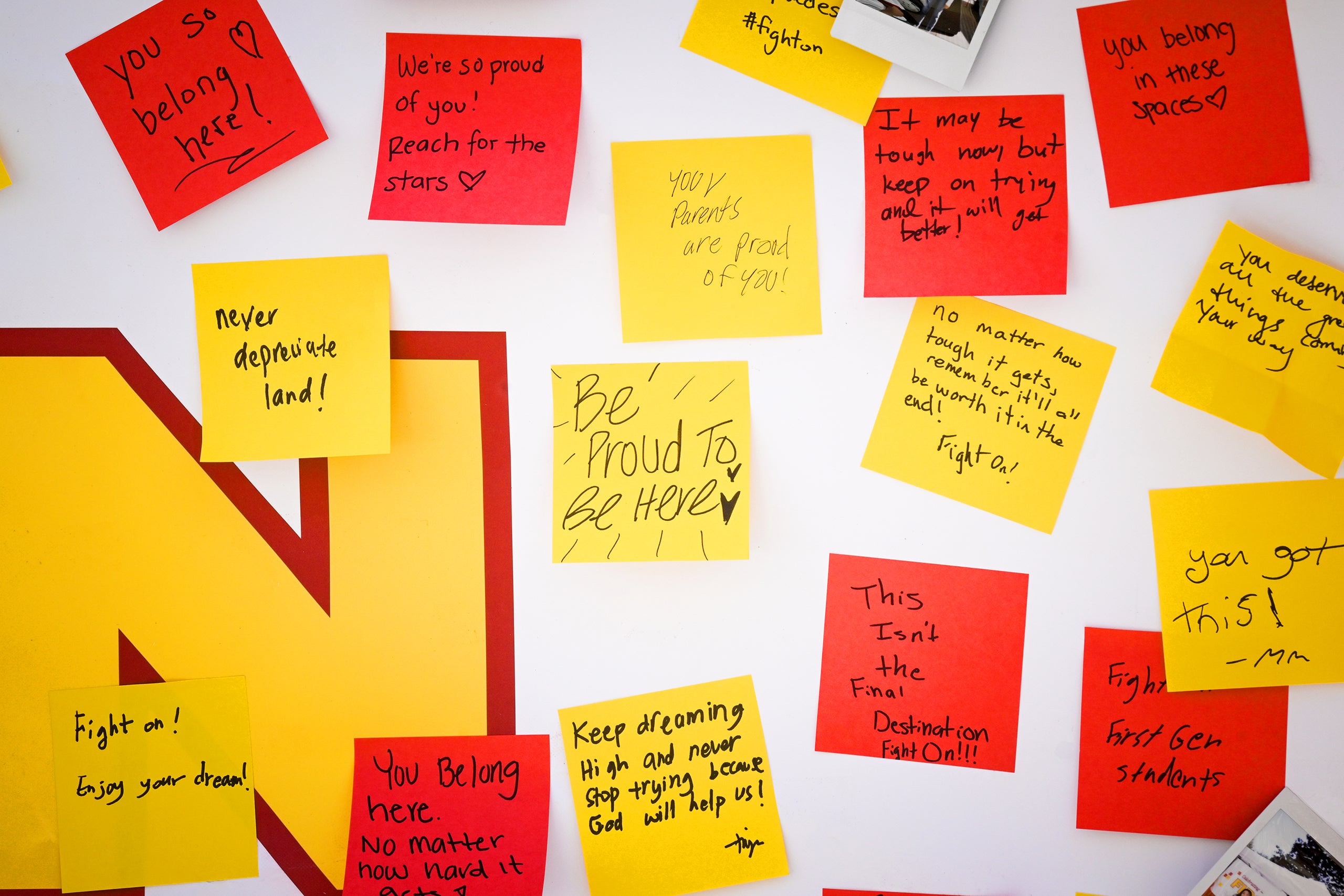 Wall with an 'N' design covered in sticky notes with messages of encouragement and belonging, alongside photos.