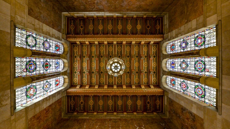 Ornate ceiling with stained glass windows and intricate patterns in a historic, stone-walled room.