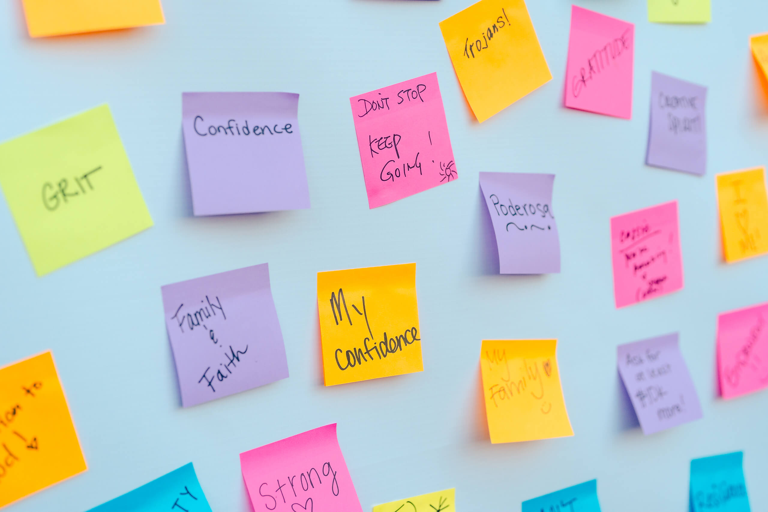 A board with colorful sticky notes displaying motivational words like 'GRIT,' 'CONFIDENCE,' 'FAMILY and FAITH,' 'STRONG,' 'GRATITUDE,' and 'KEEP GOING!' in various handwriting.