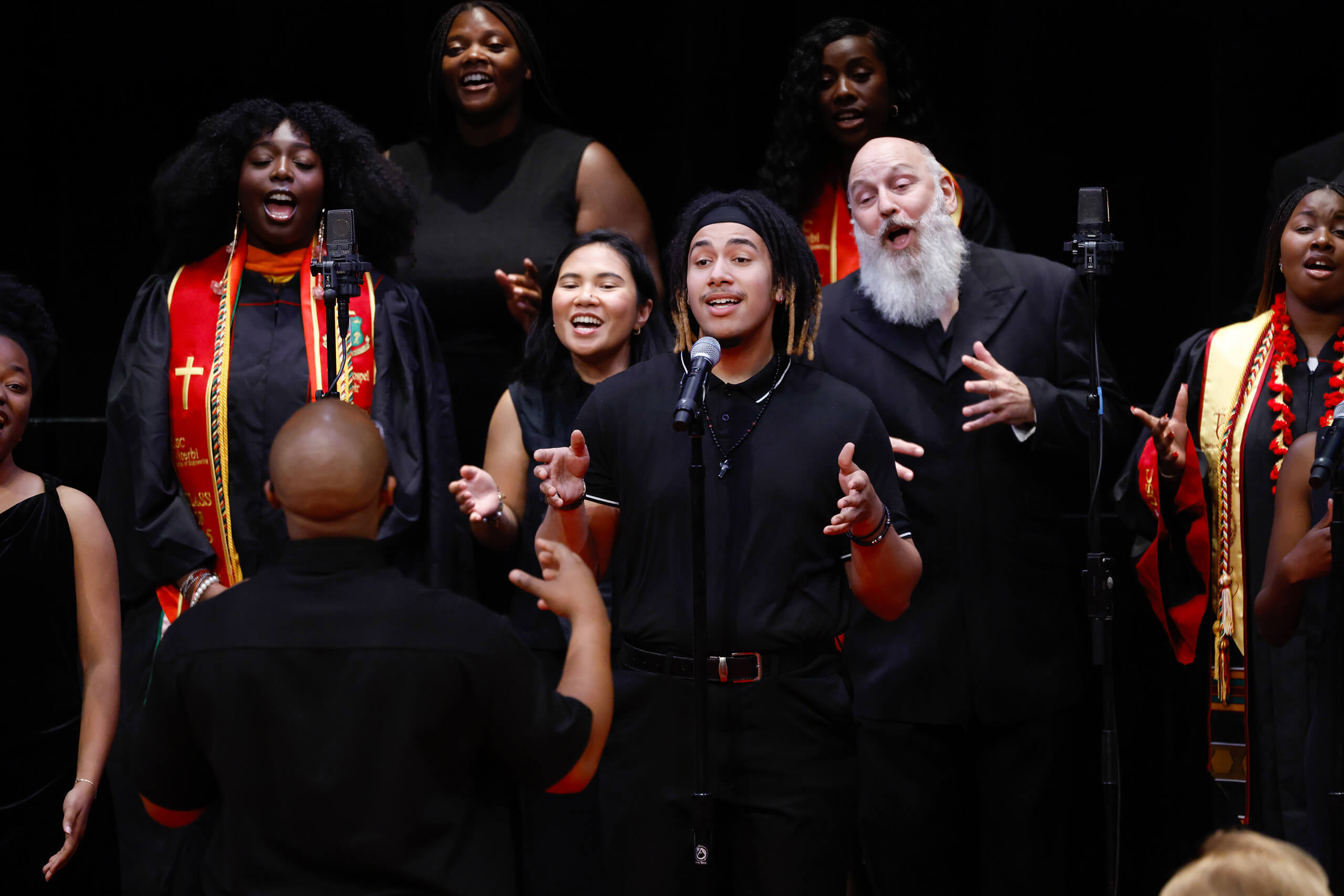 A choir in black and red regalia sings passionately at the 2025 USC Baccalaureate in Bovard Auditorium.