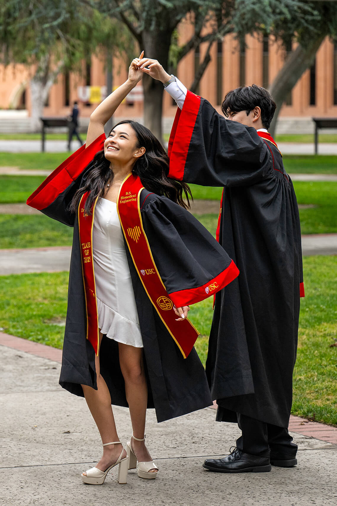 A USC graduate in red and gold regalia dances with a friend on campus during the 2025 commencement celebration.