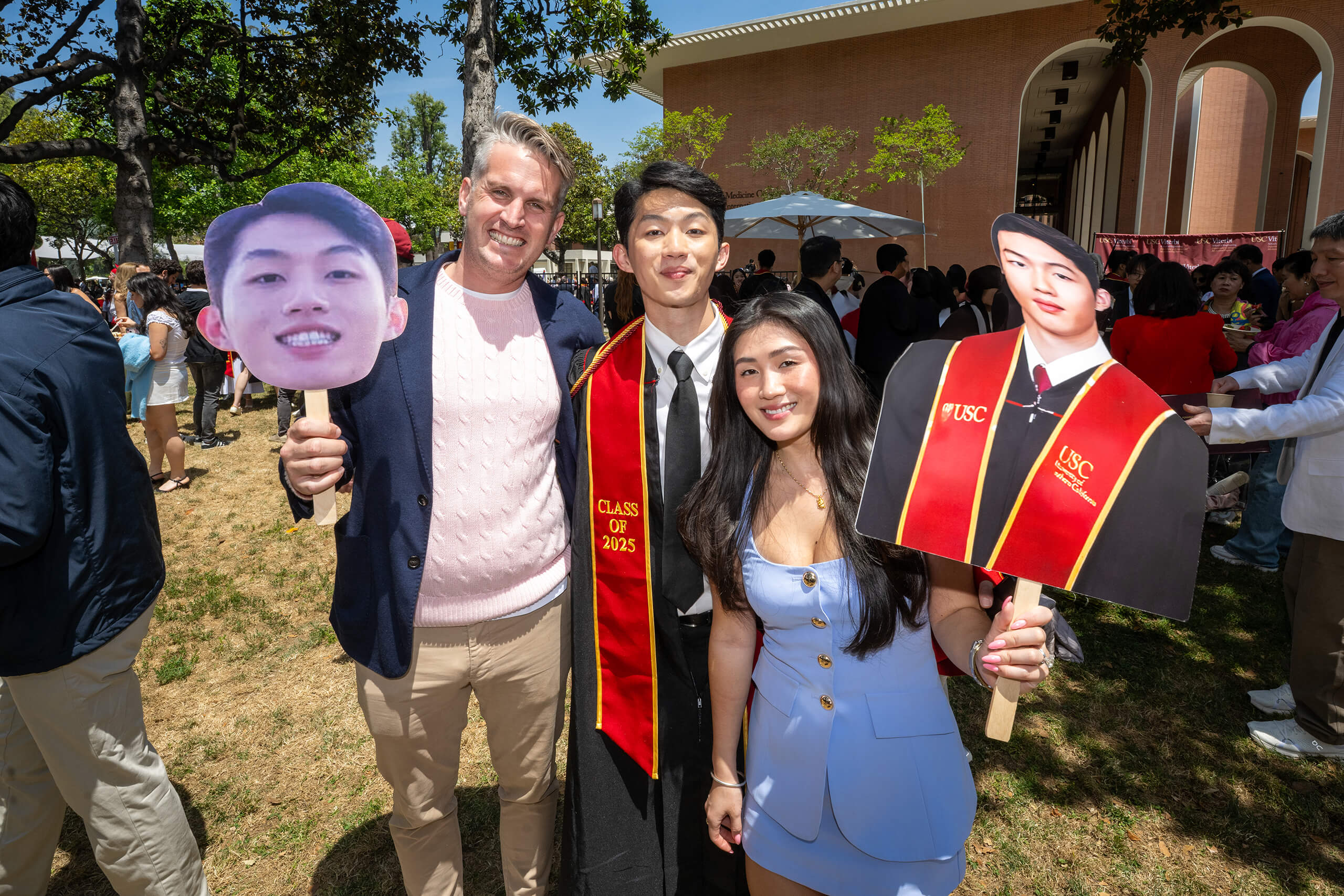 Family poses with a graduate in USC regalia and large photo cutouts of the graduate at the 2025 commencement celebration on campus.