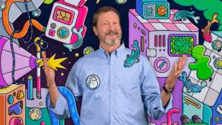 Scott Fraser stands with his hands up surrounded by various brightly illustrated objects