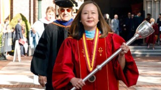 Tracy Tambascia walking in commencement with a silver torch