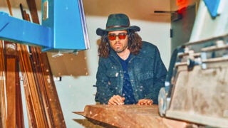 Taylor Donsker designing furniture while wearing black and red sunglasses and a jean jacket and hat