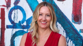 Nadine Watt smiling and wearing a red shirt with a red, white and blue graffiti wall background