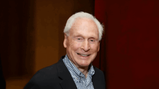 Malcolm Currie smiling in front of a cardinal background