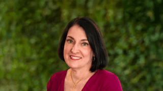 Ida Clair smiling and wearing a red shirt in front of a blurred green background